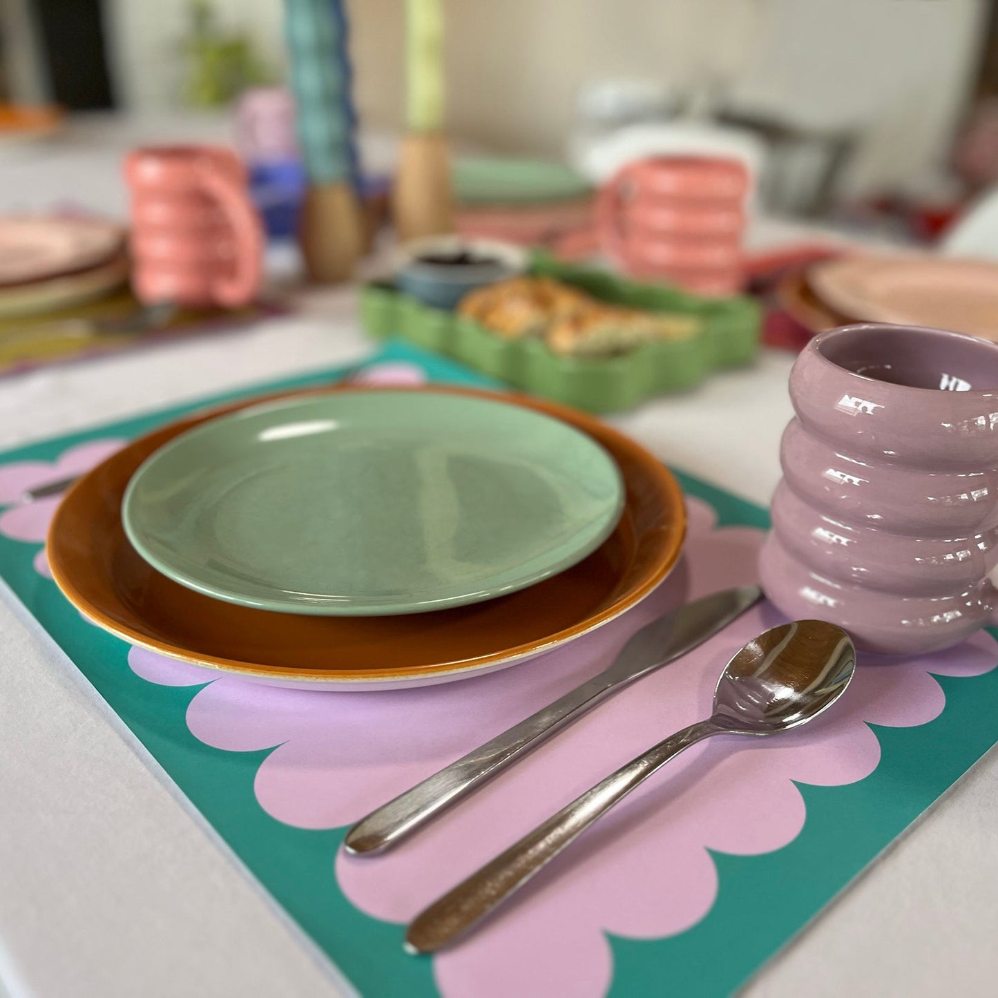 Table setting with plates, mugs, and cutlery on a colorful scallop paper placemat.