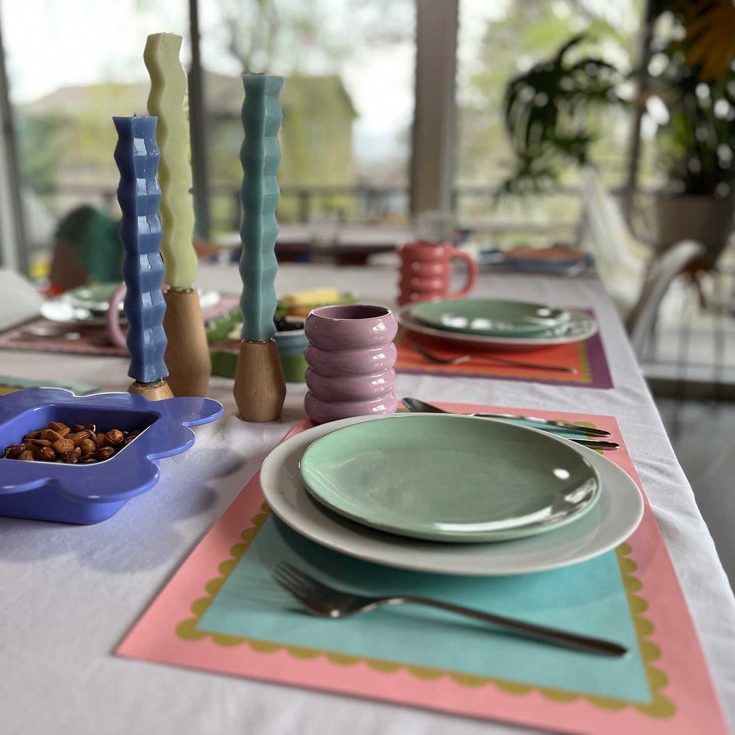 Colorful table setting with plates, bowls, and utensils on a blue and pink scallop paper placemat.
