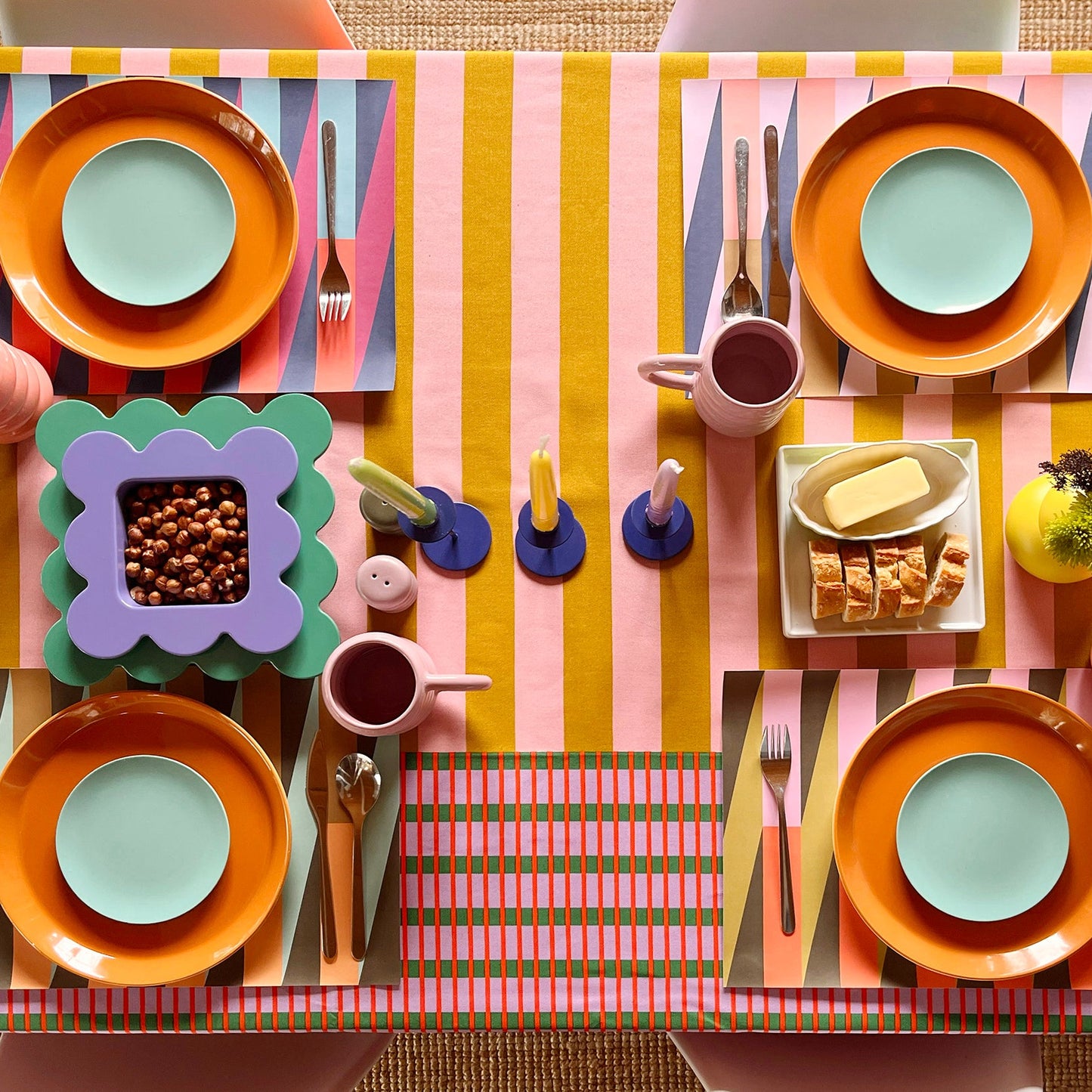 Colorful table setting with striped tablecloth and colorful paper placemats, orange plates, and blue bowls.