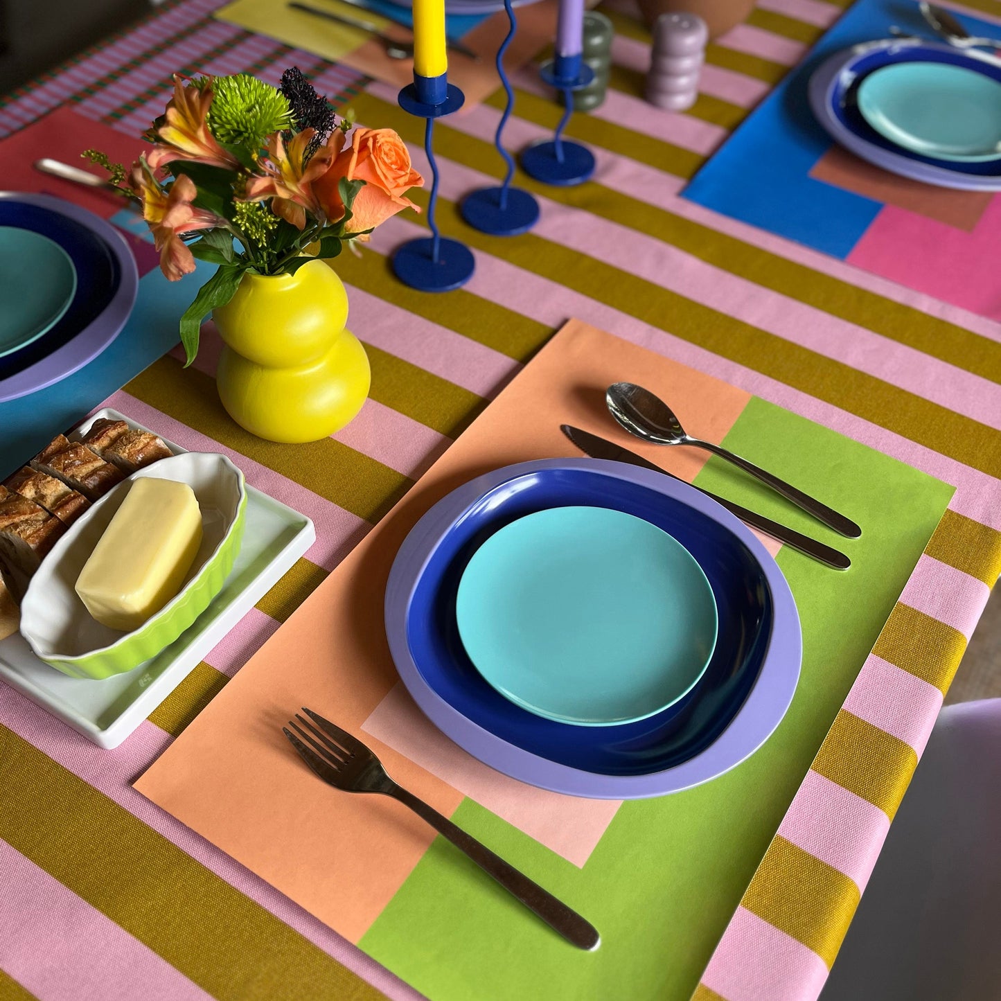 Colorful table setting with paper placemats, plates, and cutlery.