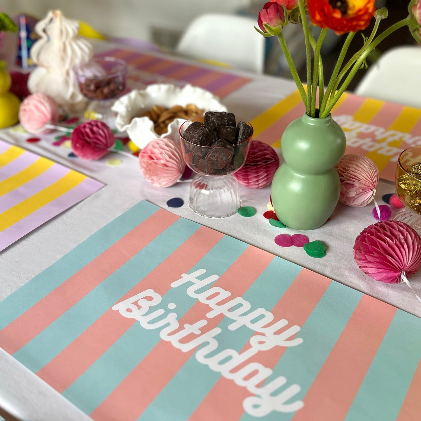 Decorated birthday table with striped birthday paper placemats, flowers, and balloons.