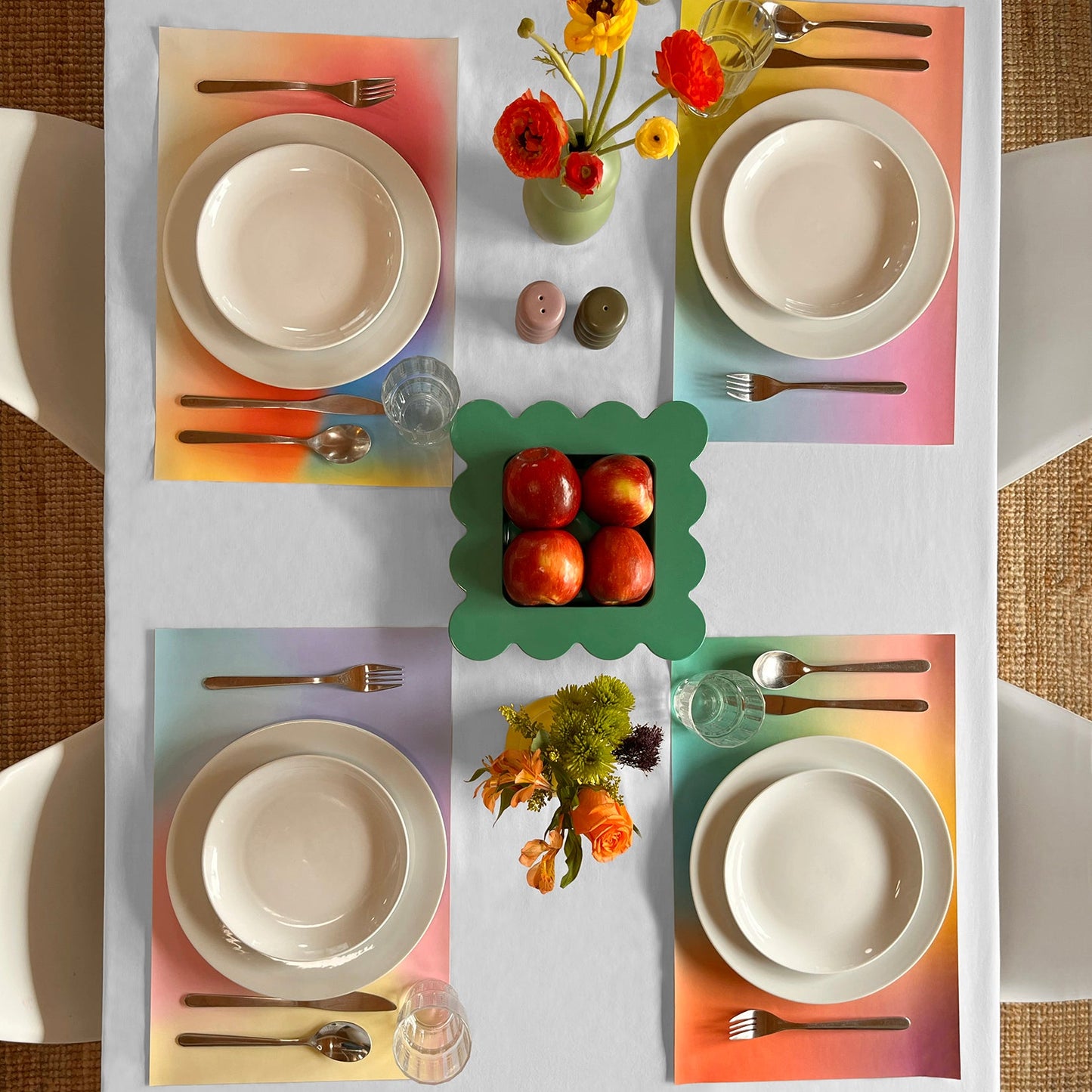 Table setting with colorful paper placemats, plates, and floral arrangements on a white tablecloth.