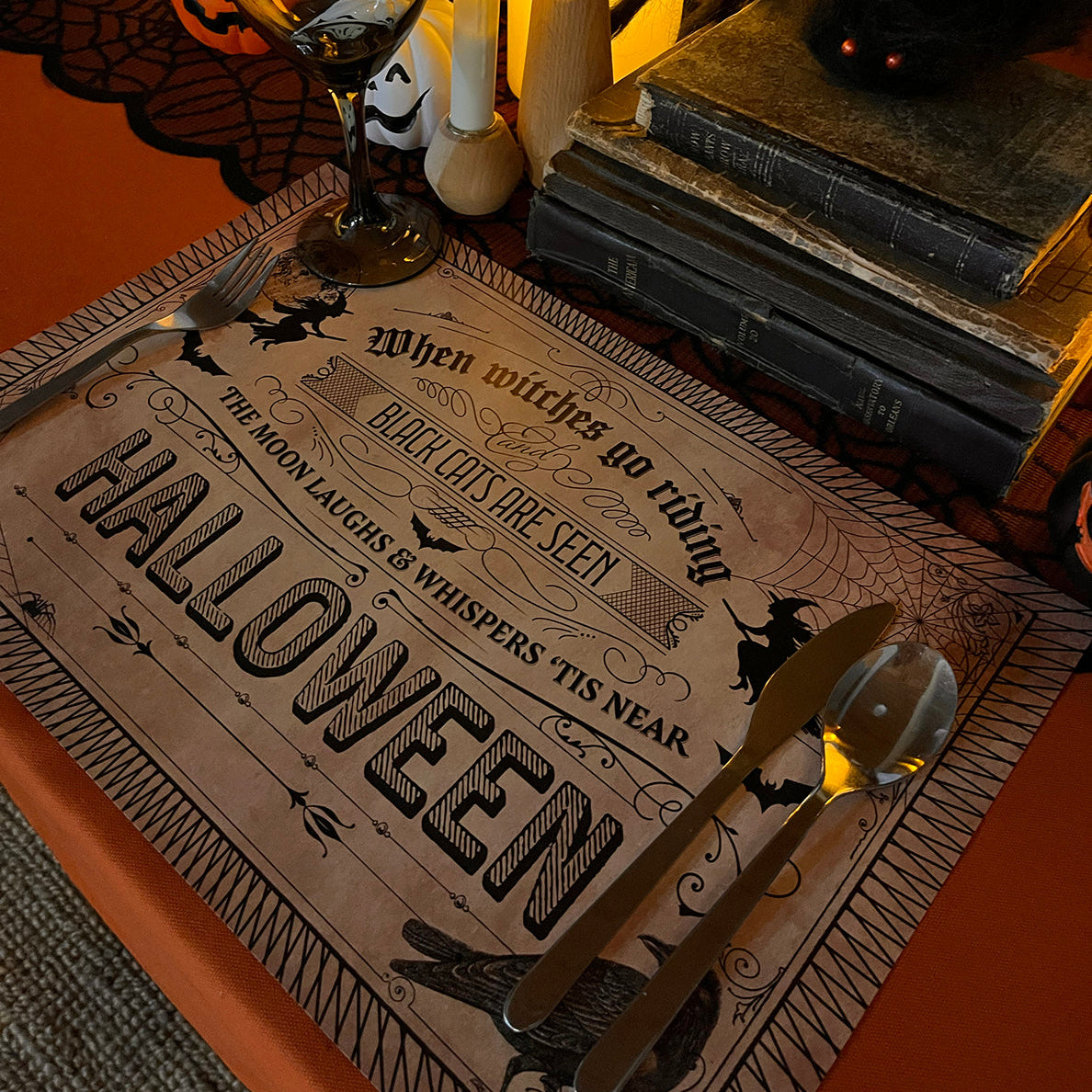 Halloween-themed table setting with candles, vintage looking paper placemat, and books.