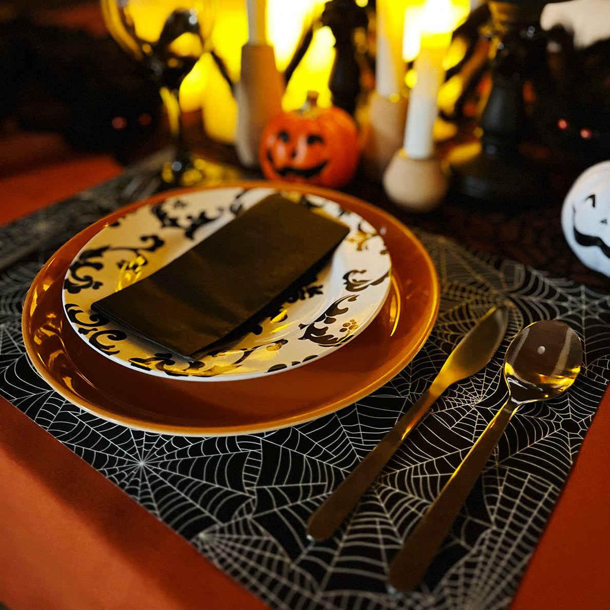 Halloween-themed table setting with candles, pumpkins, and decorative spider web paper placemats.