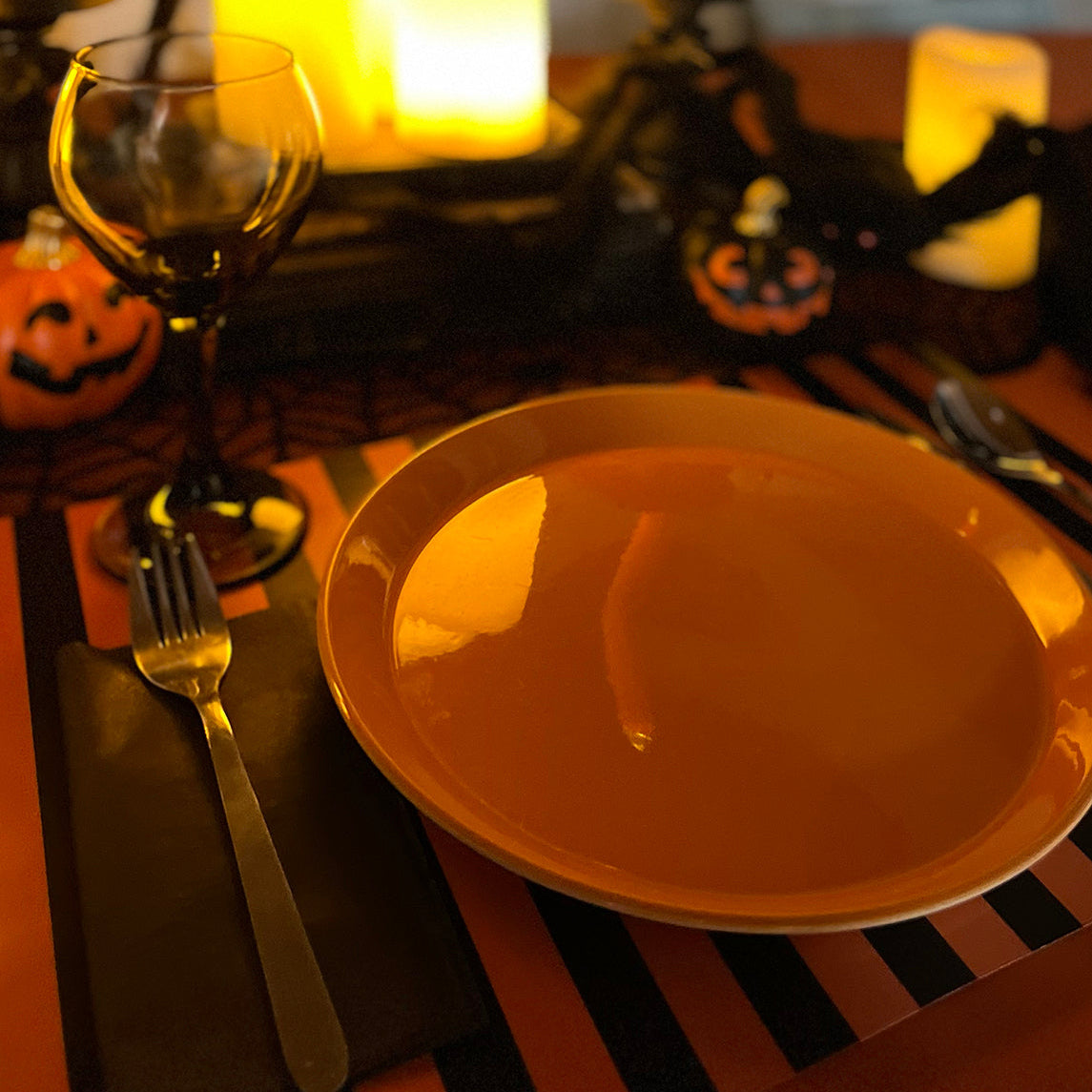 Halloween-themed table setting with candles, pumpkins, and striped paper placemat.