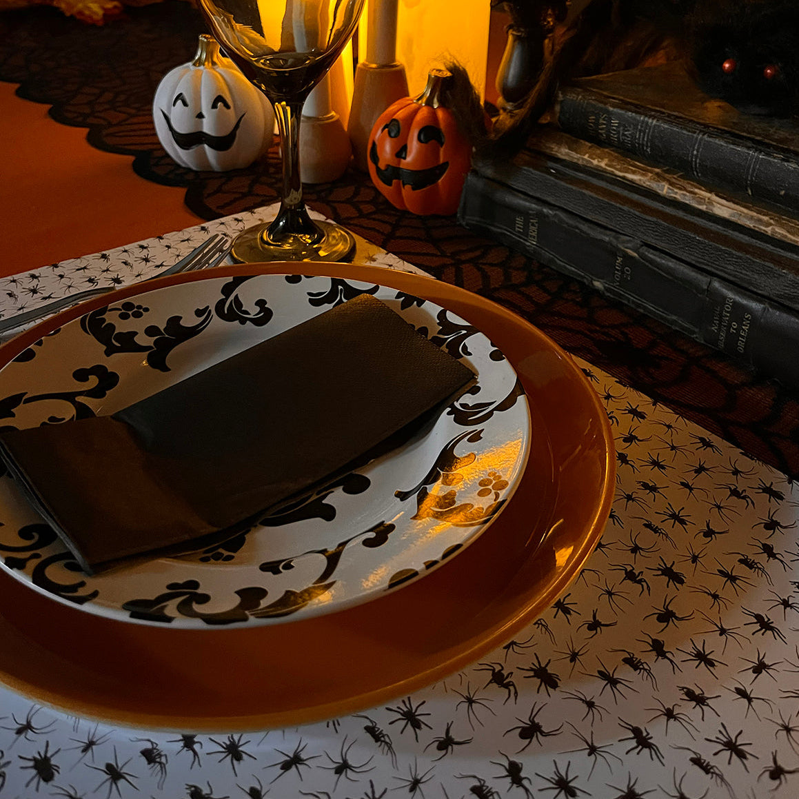 Halloween-themed table setting with candles, pumpkins, and spider paper placemats.