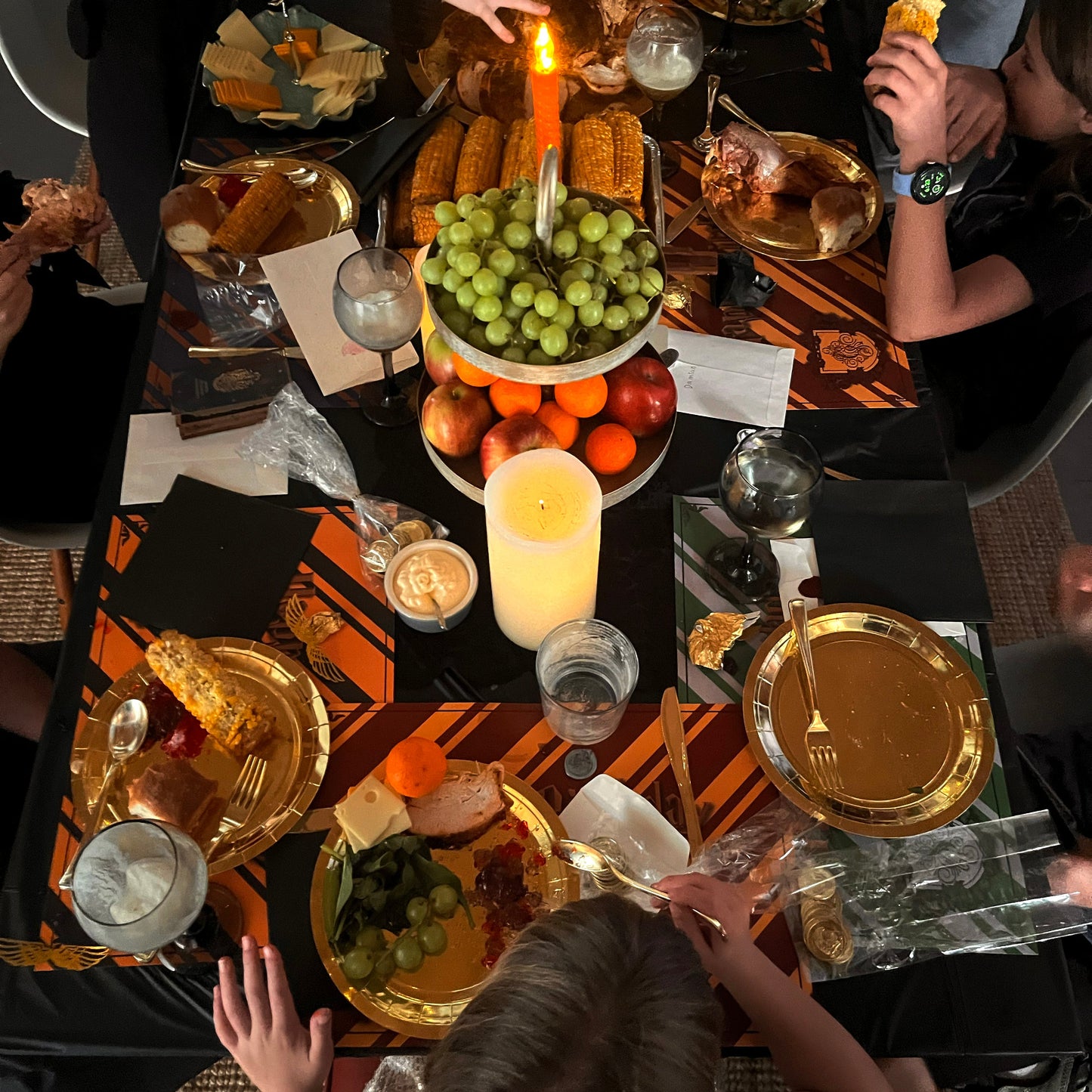 Dining table set for a meal with candles, plates, and birthday paper plates, surrounded by people.