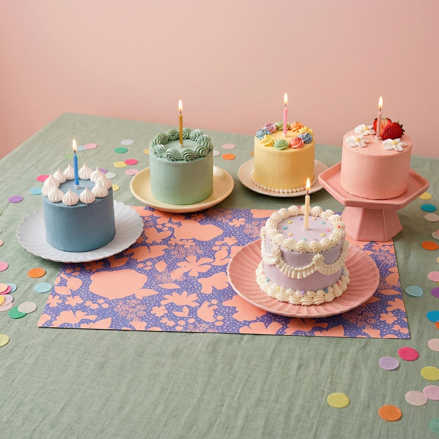 Cakes on a floral paper placemat set for a party on a green tablecloth.