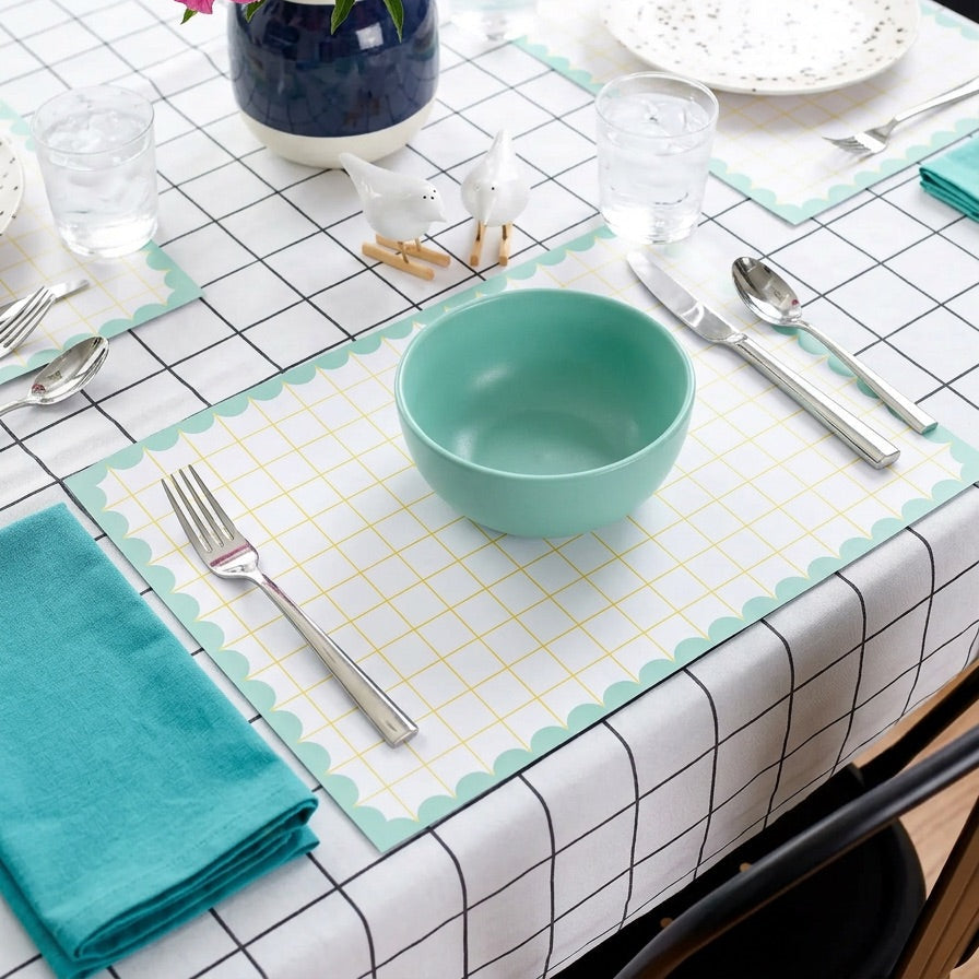 Dining table setting with teal bowl, pink flowers, and checkered grid paper placemats.