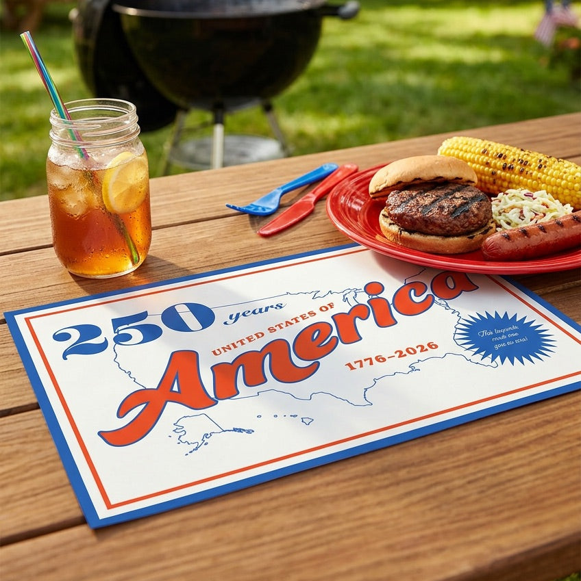 Outdoor barbecue scene with a grill, food, and drink on a table with an 'America' paper placemat.