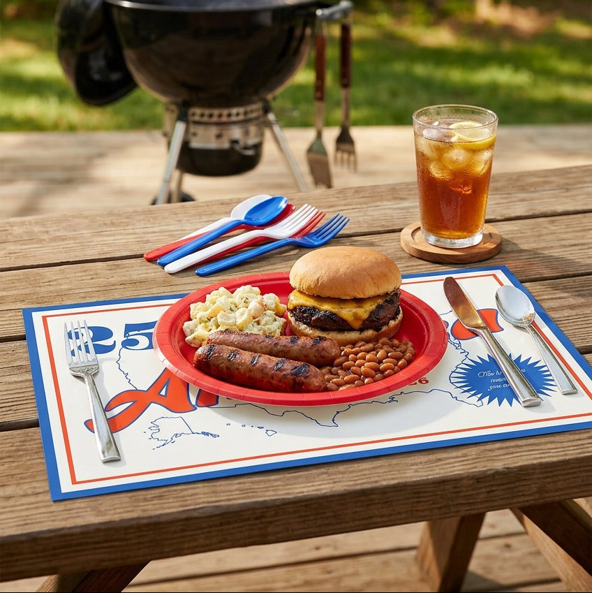 Outdoor setting with a grill, table, and meal on a paper placemat with American flag decorations.