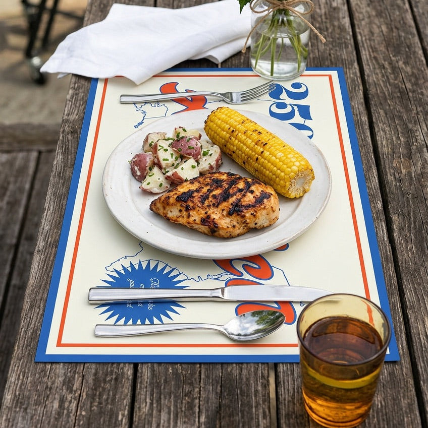 Outdoor dining setup with a plate of food, glass of beer, and flowers on a patriotic paper placemat