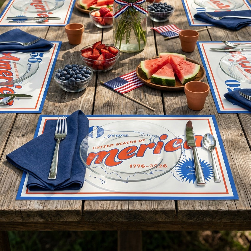 Outdoor table setting with July 4th theme, including American flags, flowers, and watermelon.