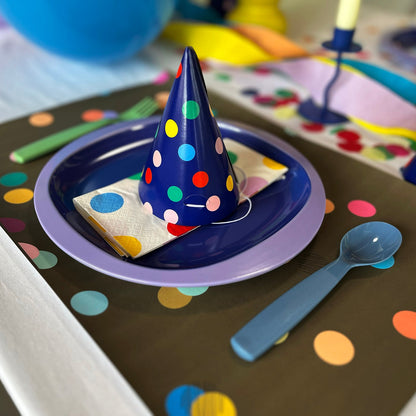Children's party table setting with colorful polka dot paper placemats and hats and plates.
