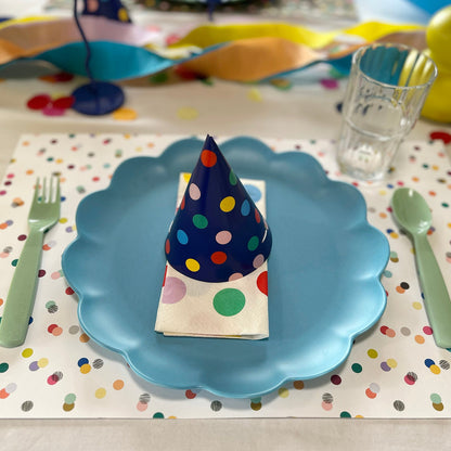 Table setting with a blue plate, colorful polka dot napkin, and cutlery on a polka dot placemat.