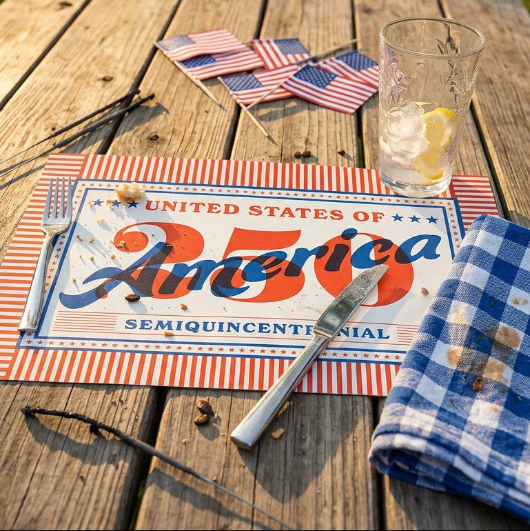 Outdoor setting with a table set for a celebration, featuring a 'United States of America 250' paper placemat.