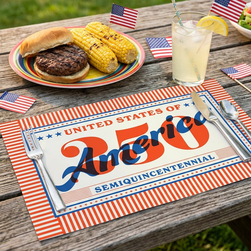 Outdoor setting with a table featuring a meal, drink, and paper placemat celebrating the 250th anniversary of the United States.
