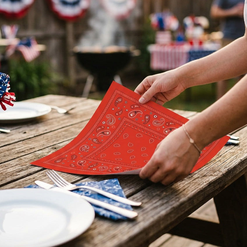 Person setting a table with red bandana paper placemats outdoors during a celebration.