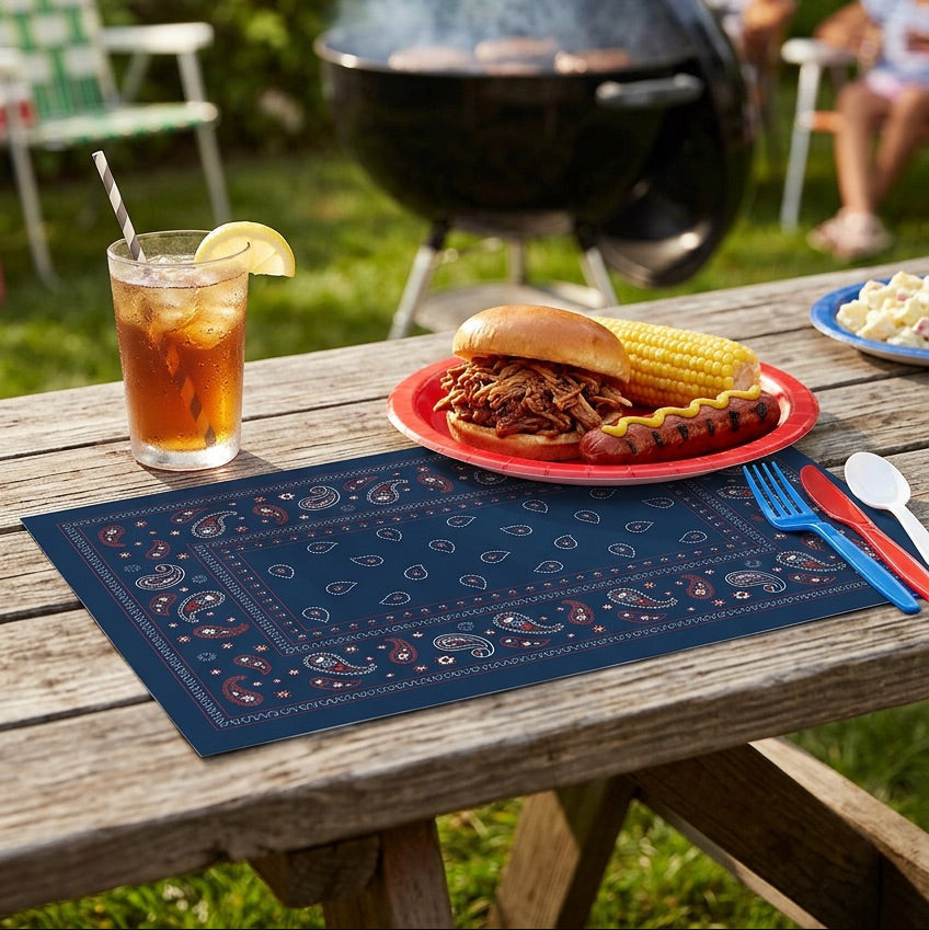 Outdoor barbecue scene with a plate of food, drink, and utensils on a wooden table.
