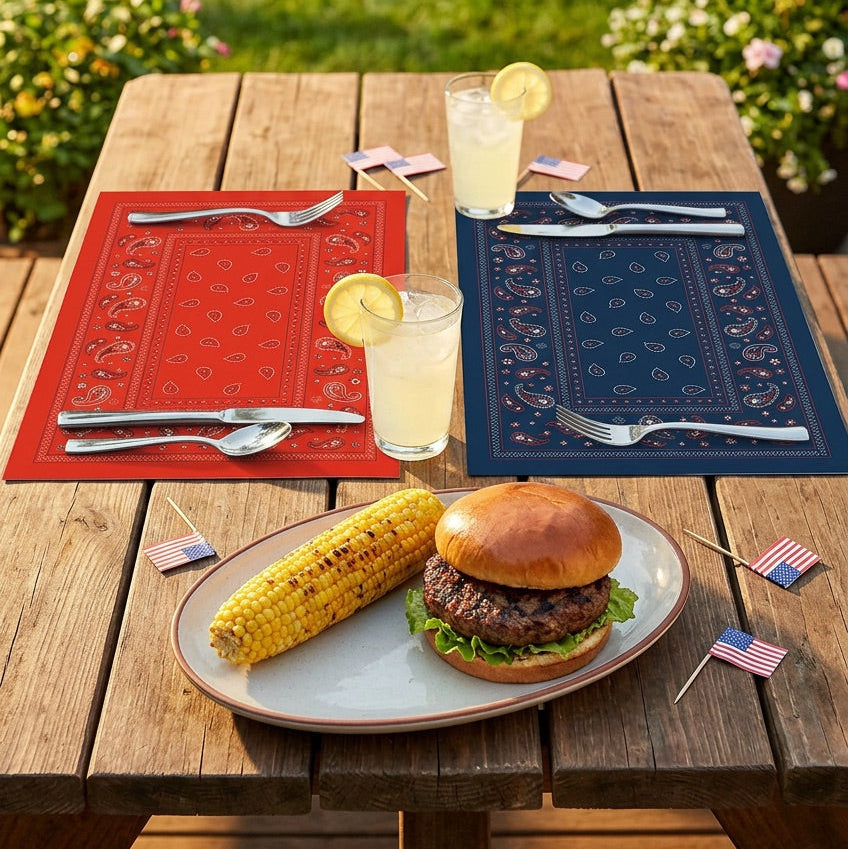 Outdoor setting with a burger, corn on the cob, and drinks on a wooden table with patriotic paper placemats.