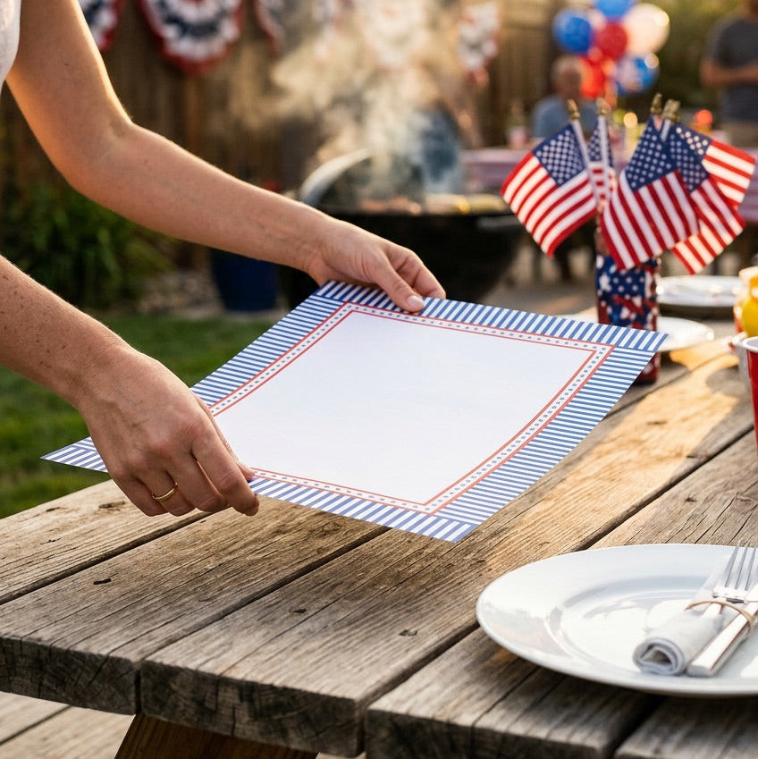 Person setting a table with American flags and a decorative paper placemat outdoors.