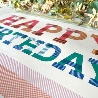 Colorful 'Happy Birthday' text on a decorative card with ribbons and tinsel in the background.