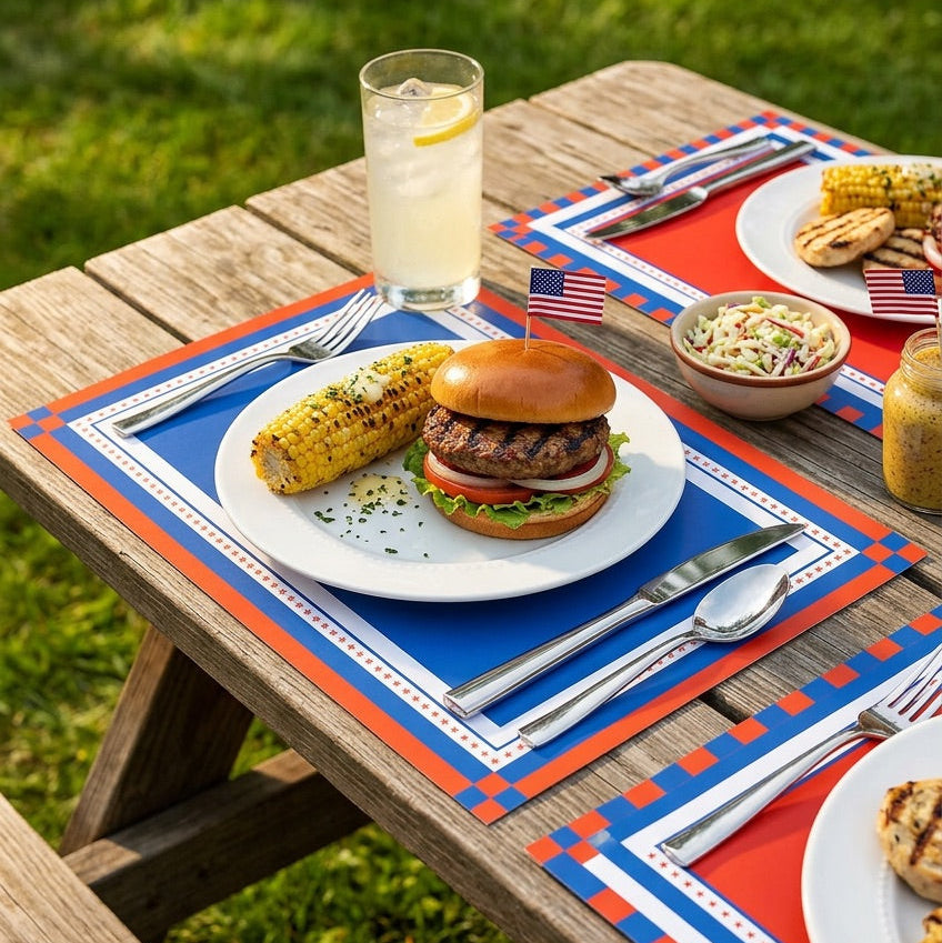 Outdoor dining setup with burgers, corn on the cob, and lemonade on a patriotic paper placemat.