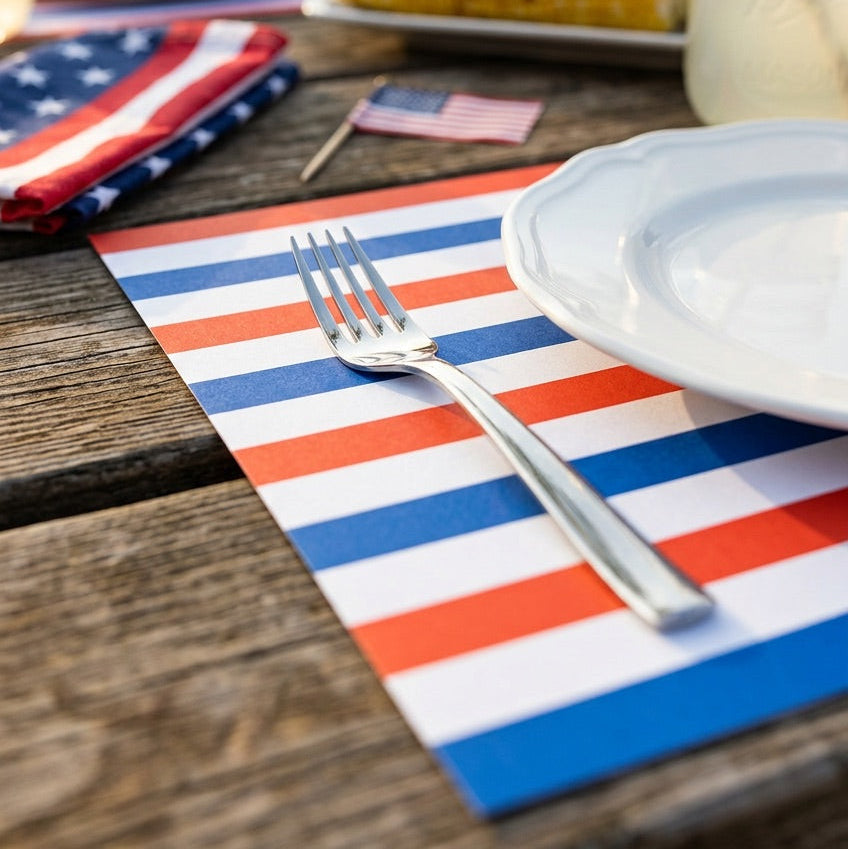 Outdoor setting with a table set for a meal, featuring patriotic striped paper placemats and utensils.