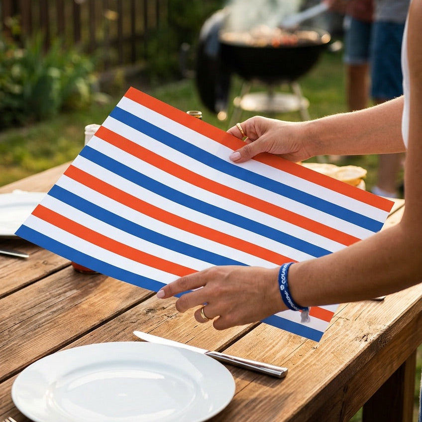 Person setting a table with a striped paper placemat in an outdoor setting