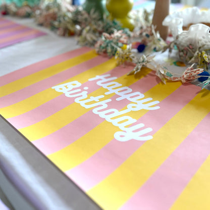Striped paper placemat with 'Happy Birthday' text on a table, decorated with flowers.