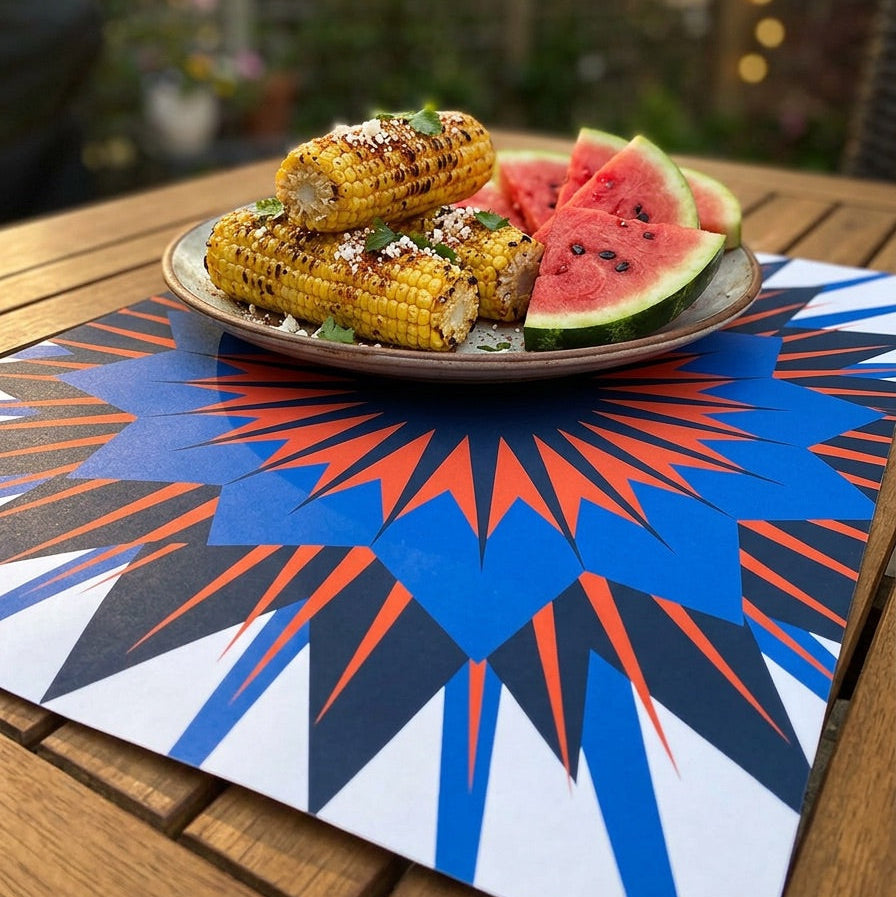 Grilled corn and watermelon on a plate with a colorful paper placemat outdoors.