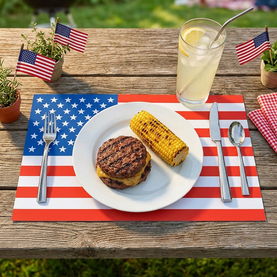Outdoor setting with a plate of food on an American flag paper placemat, surrounded by flags and a glass of lemonade.