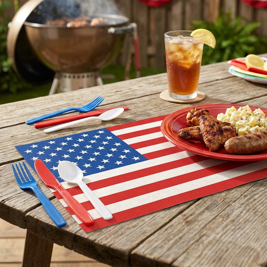 Outdoor setting with a grill, American flag paper placemat, and food on a wooden table.