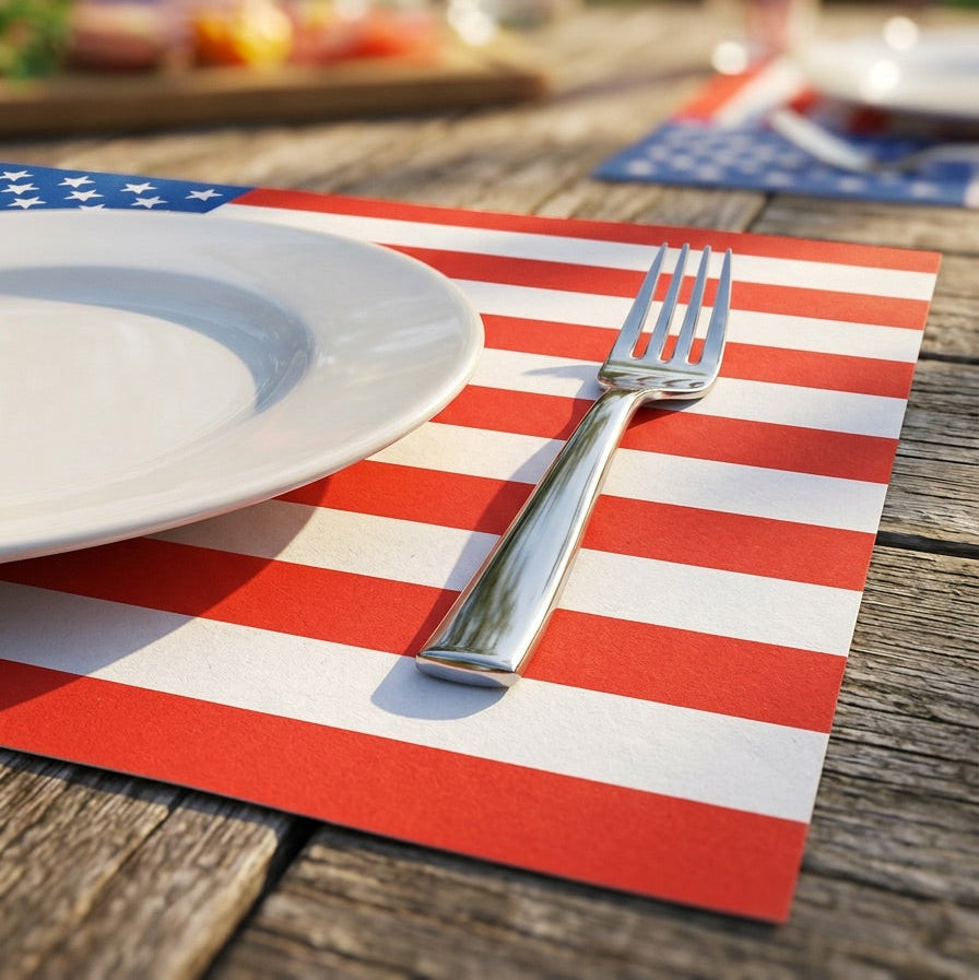 Dining setup with American flag paper placemat, plate, and fork on a wooden table outdoors.