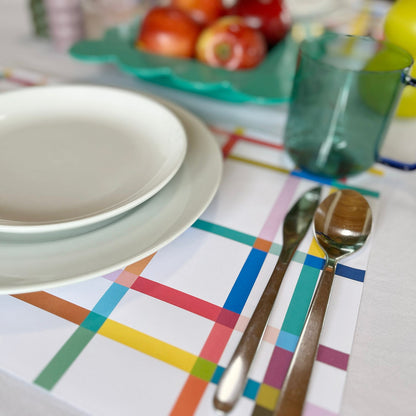 Dinner setting with plates, cutlery, and colorful paper placemat on a table.