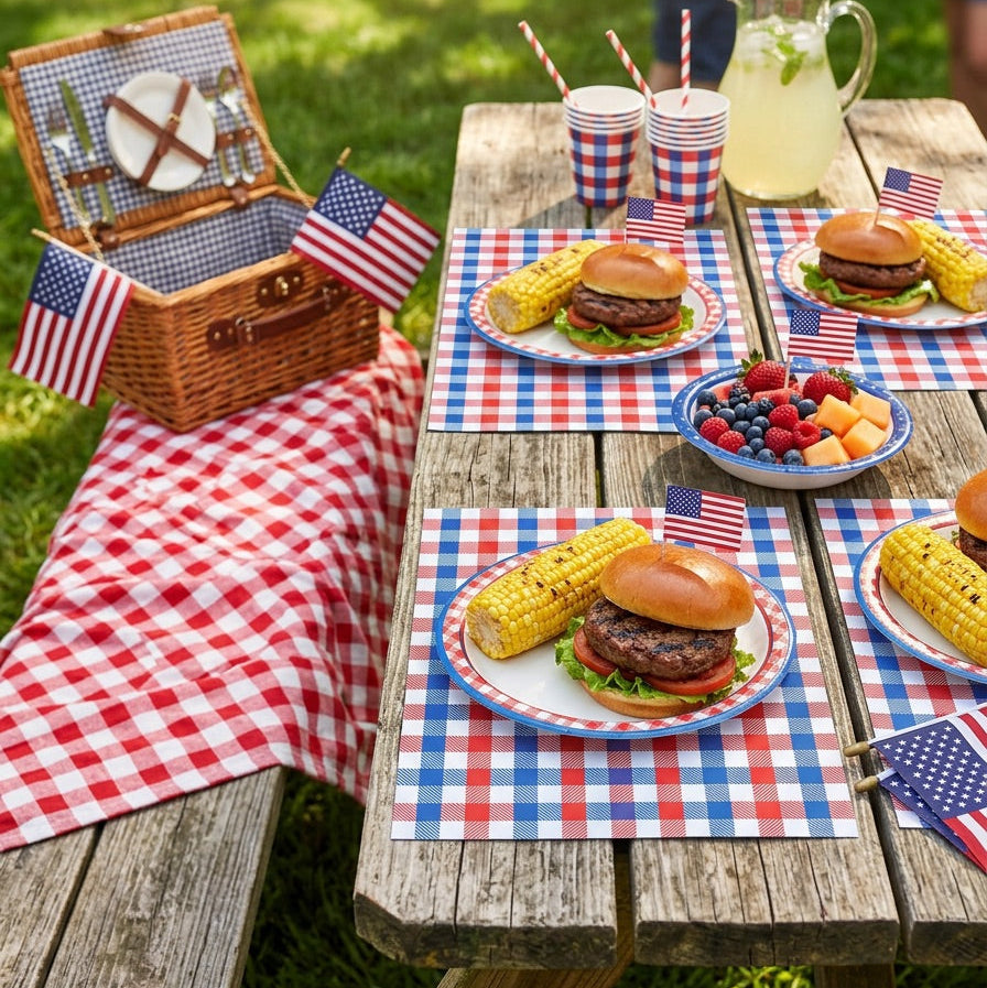 Picnic setup with burgers, corn on the cob, and fruit platter on a checkered paper placemat with American flags.