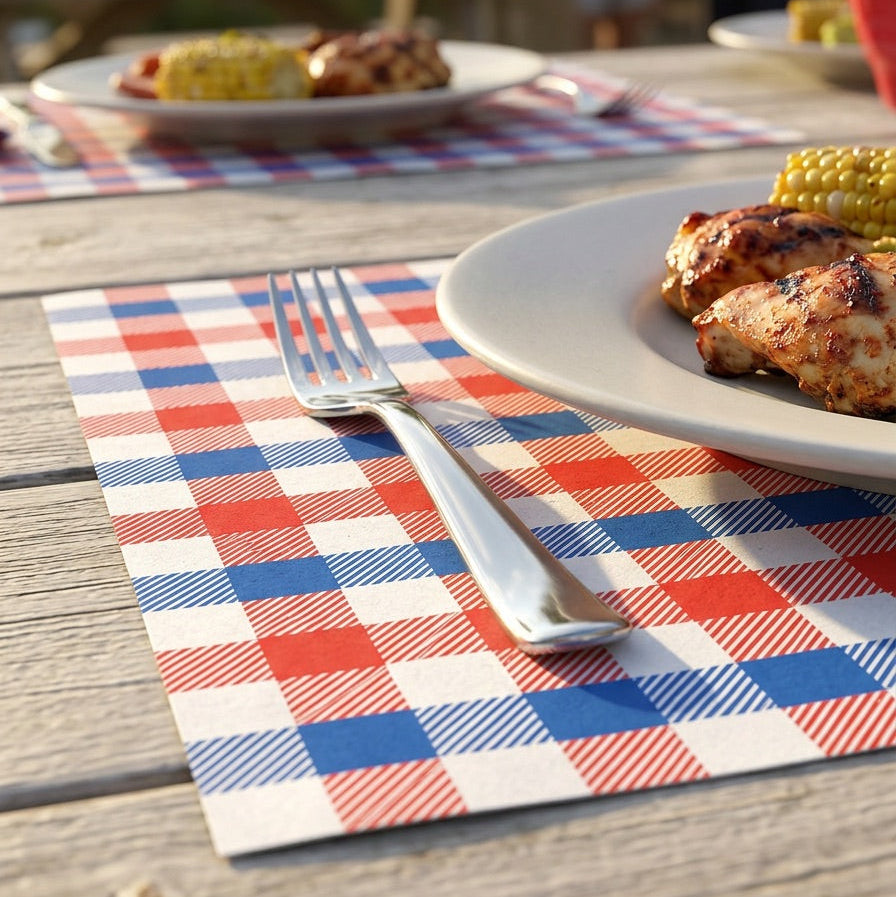 Outdoor setting with plates of food on a checkered paper placemat, people in the background.