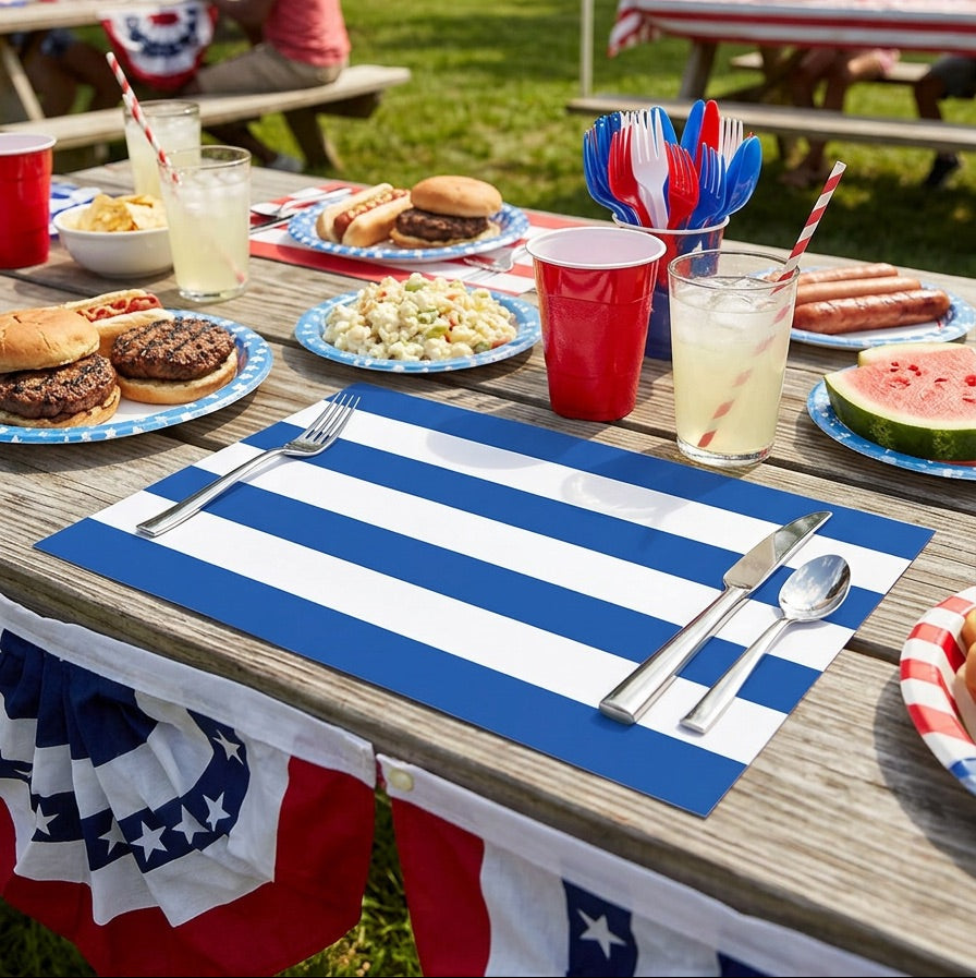 Outdoor picnic scene with food, drinks, and striped paper placemats on a wooden table.