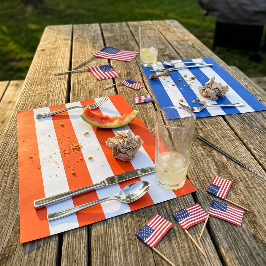 Outdoor table setting with American flags, glasses, and food on striped paper placemats.