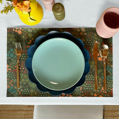 Table setting with a decorative paper placemat, blue plate, and floral pattern.