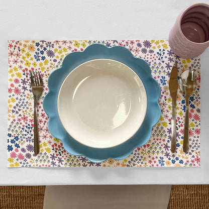 Dinner set with blue bowl, pink mug, floral paper placemat on a white table.