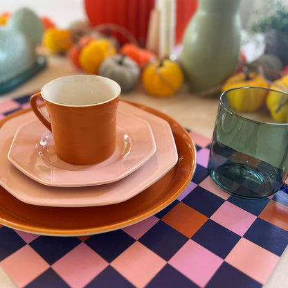 Colorful ceramic tableware set on a checkered paper placemat with pumpkins in the background