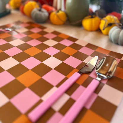 Checkered paper placemat with pink cutlery on a table with pumpkins and decorative items in the background.