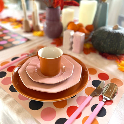 Table setting with polka dot paper placemat, orange and pink dishes, and pink cutlery.