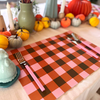 Checkered placemat with pink and brown colors on a table set with pumpkins and utensils.