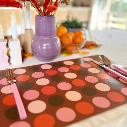 Polka dot paper placemat with pink cutlery on a table setting.