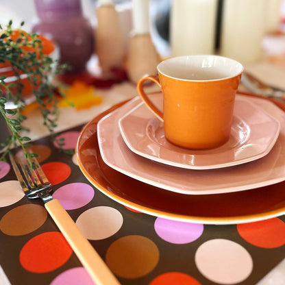 Colorful table setting with an orange cup on a polka dot paper placemat.