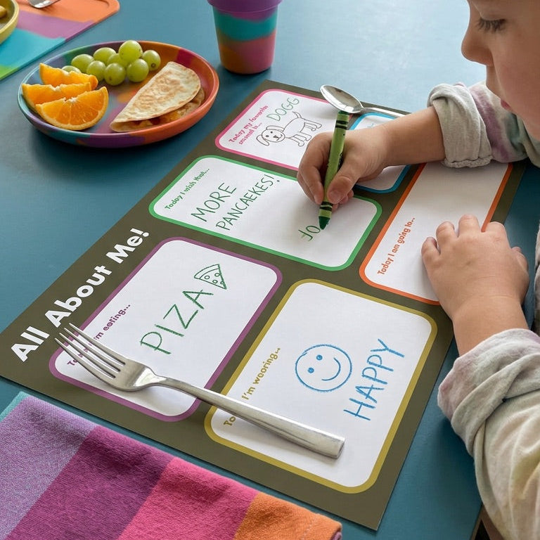 Child at a table with a 'All About Me' activity sheet, colorful placemat, and snacks.