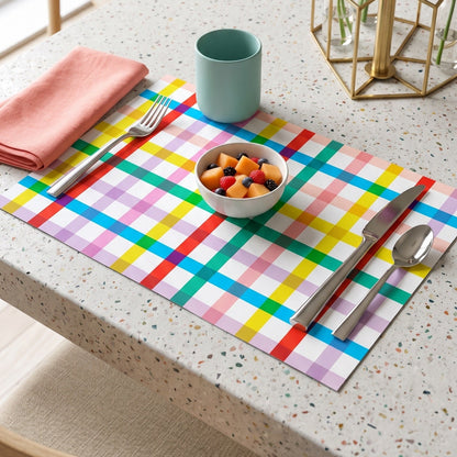 Colorful checkered paper placemat on a table with a bowl of fruit, cup, and flowers.