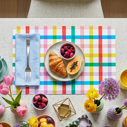 Colorful table setting with a plate of food, fruits, and flowers on a checkered paper placemat.